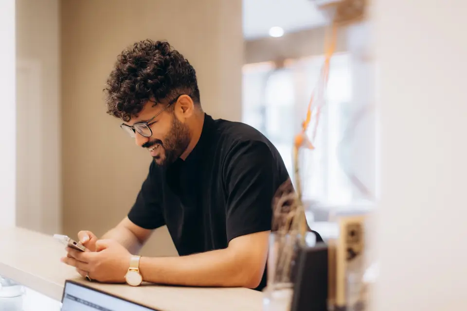A smiling man filling in a form on his phone at work