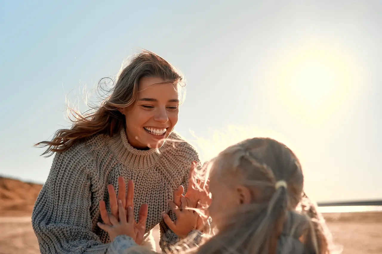 A mother and her young daughter playing a clapping game on the beach in the sun