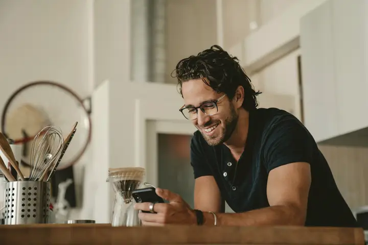 A man smiling at his phone in his kitchen during a telehealth appointment