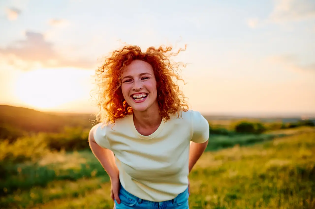 A red-haired woman laughing outdoors on a bright, sunny day