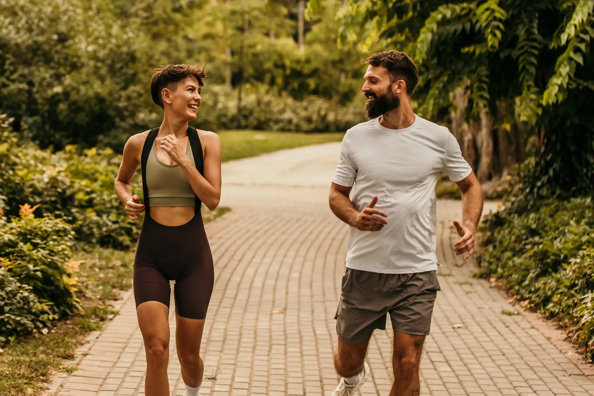 A couple laughing as they jog side by side along a park path