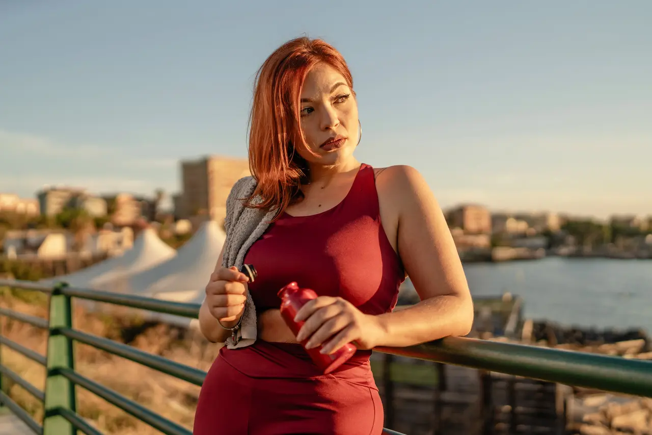 A woman catching her breath with a water bottle after a waterfront workout