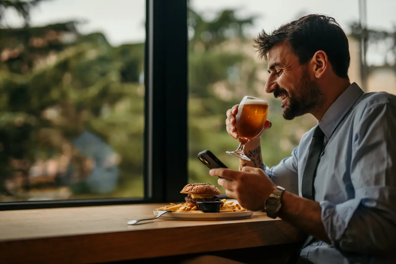 A man smiling over a burger and a beer on his lunch break