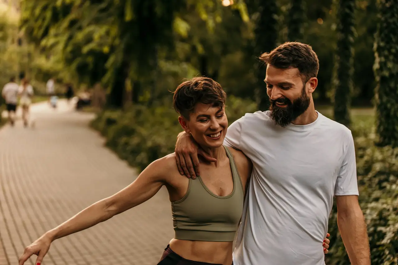 A couple laughing as they walk arm in arm through a leafy park